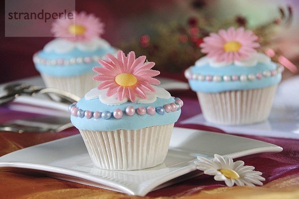 Hellblaue Cupcakes mit rosa Blüten und Zuckerperlen