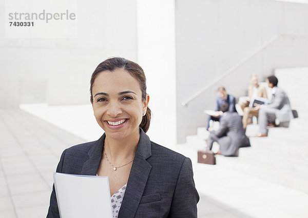 Porträt einer selbstbewussten Unternehmerin mit Mitarbeitern im Hintergrund