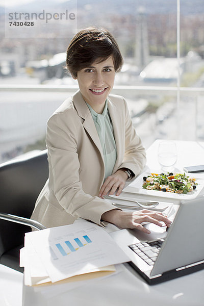 Porträt einer lächelnden Geschäftsfrau beim Essen und Arbeiten am Schreibtisch
