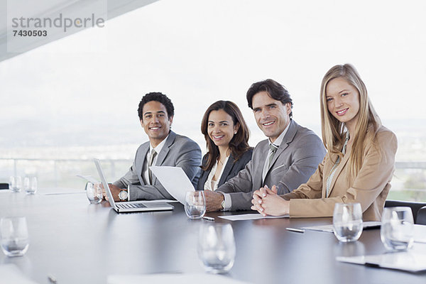 Portrait von lächelnden Geschäftsleuten  die in einer Reihe im Konferenzraum sitzen.