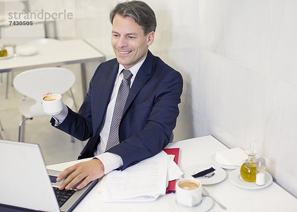 Lächelnder Geschäftsmann trinkt Kaffee und benutzt Laptop im Restaurant