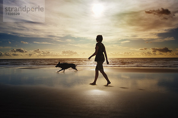 Silhouette von Frau und Hund beim Spaziergang am Strand