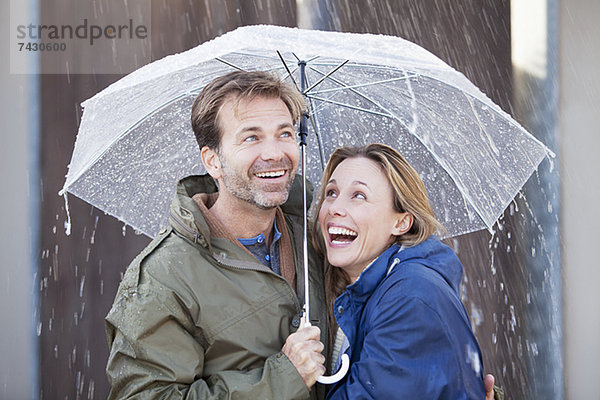 Glückliches Paar unter dem Regenschirm im Regenguss