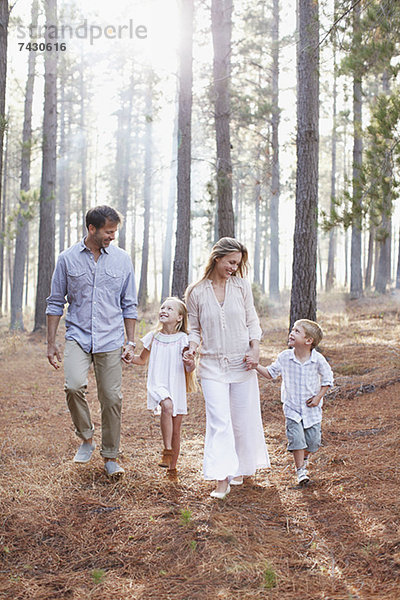 Glückliche Familie  die Händchen hält und in sonnigen Wäldern spazieren geht.