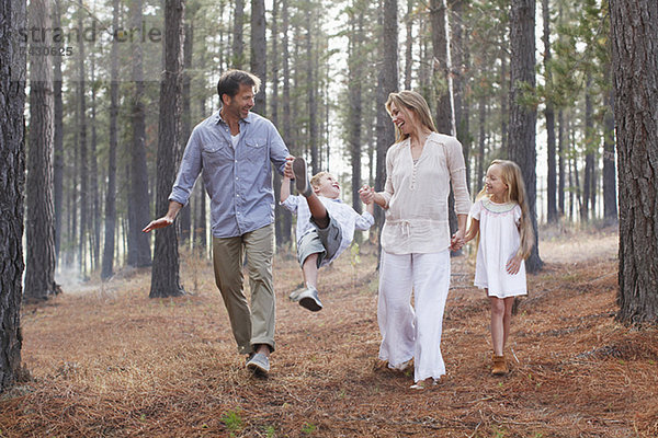 Glückliche Familie  die Händchen hält und im Wald spazieren geht.