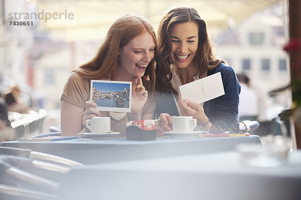 Lachende Freunde beim Betrachten von Postkarten im Straßencafé
