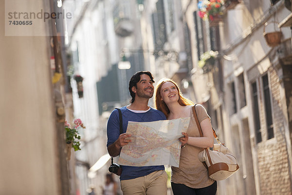 Lächelndes Paar mit Karte auf der schmalen Straße in Venedig
