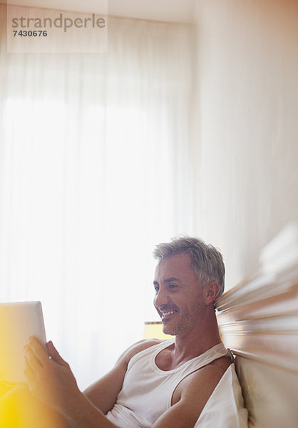 Lächelnder Mann mit digitalem Tablett im Bett