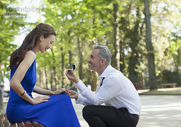 Mann mit Verlobungsring  der seiner Freundin im Park einen Antrag macht.