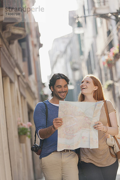 Lächelndes Paar beim Spaziergang mit Karte auf der schmalen Straße in Venedig