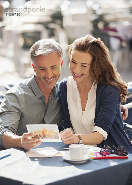 Lächelndes Paar schaut auf Postkarte im Straßencafé