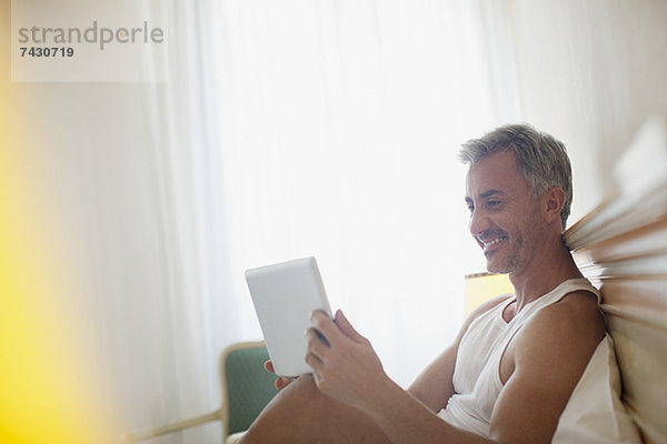 Lächelnder Mann mit digitalem Tablett im Bett