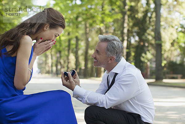 Mann mit Verlobungsring  der einer überraschten Frau einen Antrag macht.