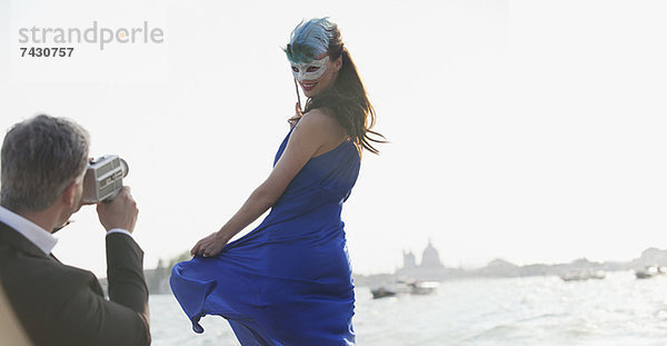 Mann filmt Frau in Maske am Wasser in Venedig