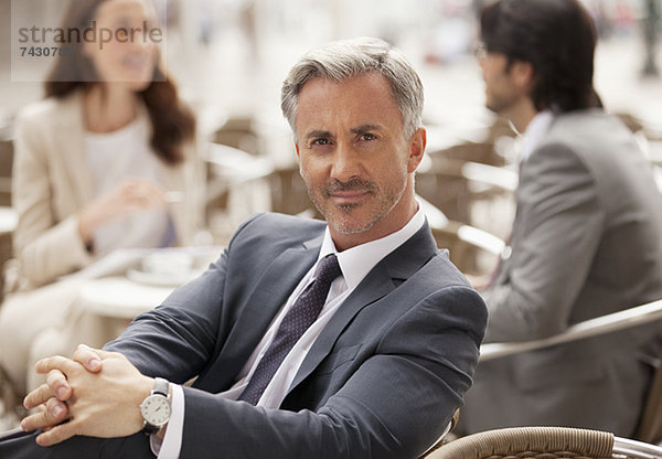 Porträt eines lächelnden Geschäftsmannes im Straßencafé mit Mitarbeitern im Hintergrund