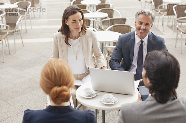 Lächelnde Geschäftsleute mit Laptop-Treffen im Straßencafé