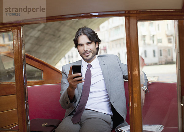 Portrait eines lächelnden Geschäftsmannes mit Handy auf dem Schiff in Venedig