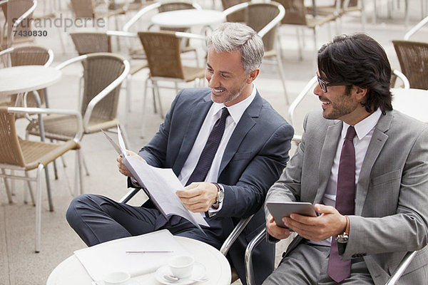 Lächelnde Geschäftsleute mit digitalem Tablett und Papierkram im Cafe