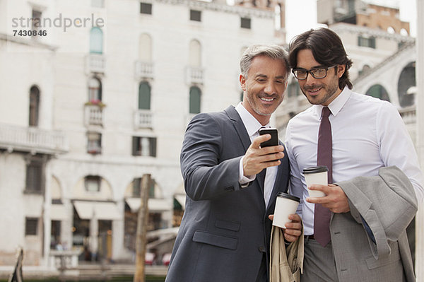 Lächelnde Geschäftsleute mit Kaffee auf dem Handy in Venedig