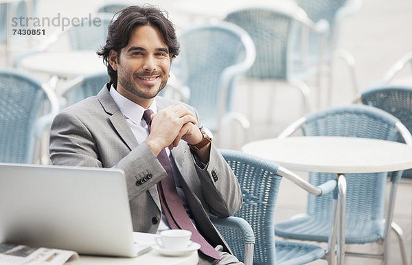 Porträt eines lächelnden Geschäftsmannes mit Laptop und Espresso im Straßencafé