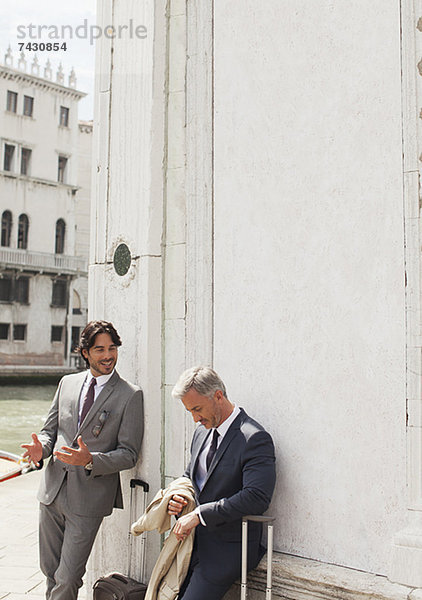 Geschäftsleute mit Koffern  die in Venedig reden und sich gegen das Bauen lehnen.