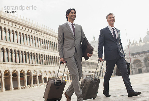 Lächelnde Geschäftsleute gehen mit Koffern durch den Markusplatz in Venedig.
