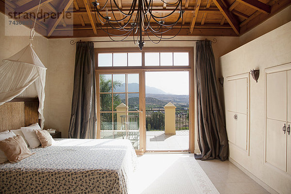 Bett mit Vordach und Fenstertüren zum Balkon im Schlafzimmer