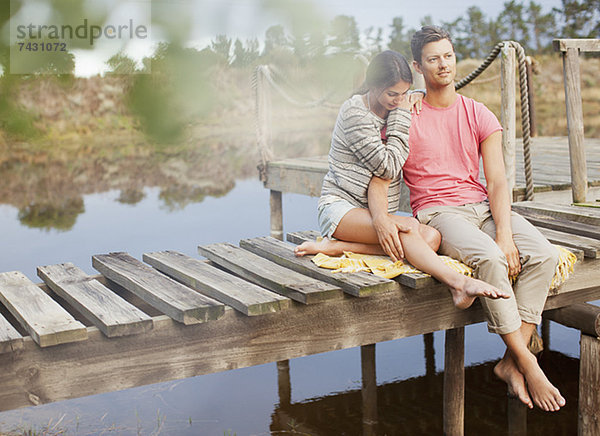Ein ruhiges Paar  das auf einem Dock über dem See sitzt.
