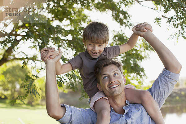 Lächelnder Vater mit Sohn auf den Schultern unter dem Baum