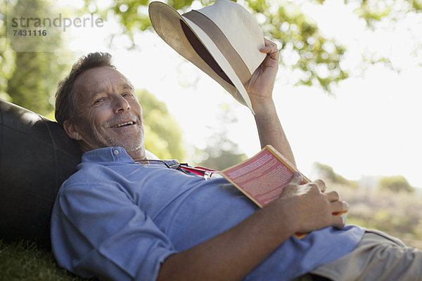 Porträt eines lächelnden Mannes auf Gras mit Buch und Hut