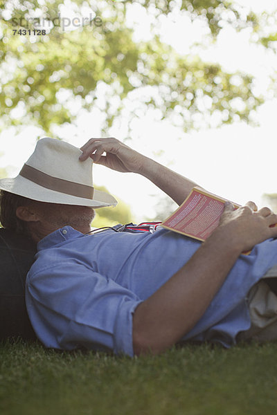 Mann schlafend im Gras mit Buch und Hutbedeckung Gesicht