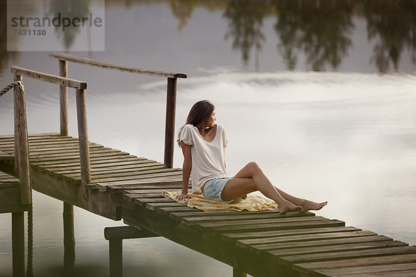 Frau auf dem Dock über dem See sitzend