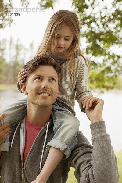 Vater trägt Tochter auf Schultern am Seeufer