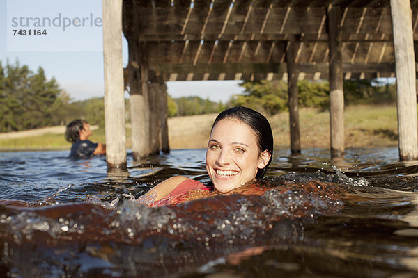 Porträt einer lächelnden Frau  die im See unter dem Dock schwimmt.