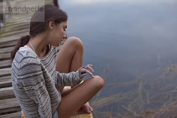 Nachdenkliche Frau auf dem Dock über dem See sitzend