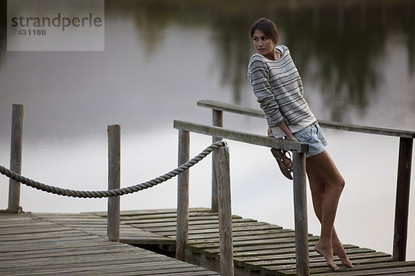 Frau  die sich auf ein Geländer am Dock über dem See stützt.