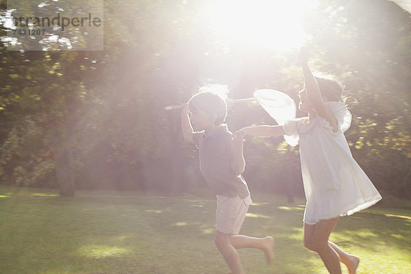 Junge und Mädchen halten sich an den Händen und laufen mit Schmetterlingsnetzen im Gras.
