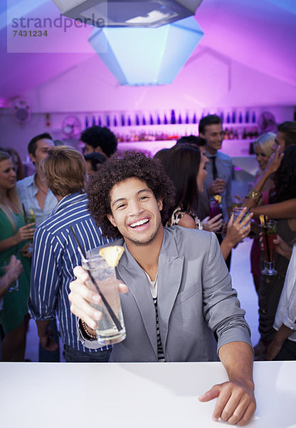 Porträt eines lächelnden Mannes mit Cocktail in der Bar des Nachtclubs