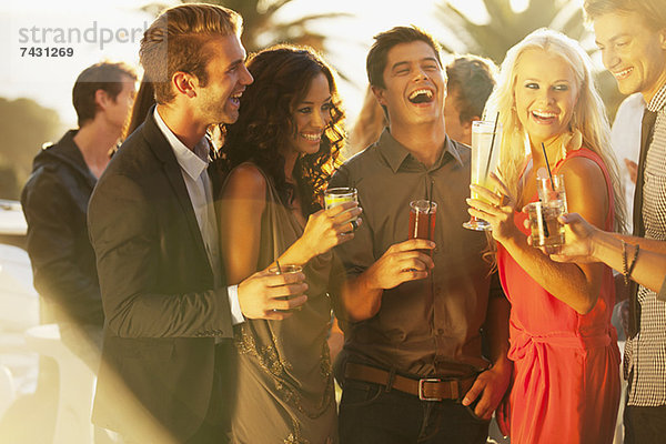 Lachende Freunde trinken Cocktails auf dem sonnigen Balkon