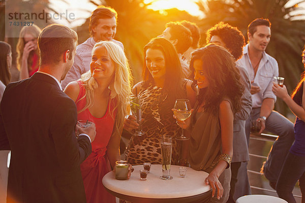 Lächelnde Freunde trinken Cocktails auf dem sonnigen Balkon