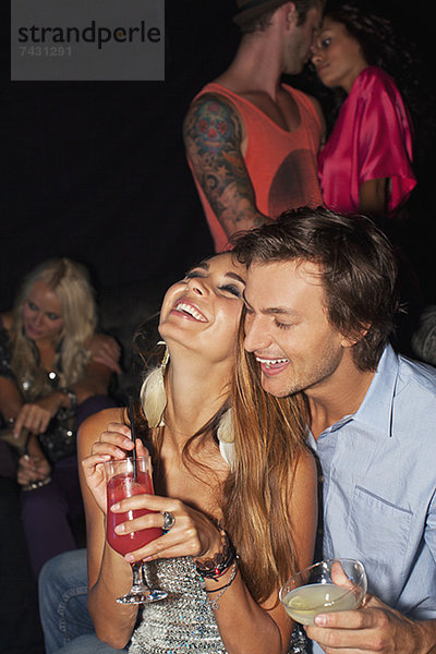Lachendes Paar beim Umarmen und Trinken von Cocktails im Nachtclub