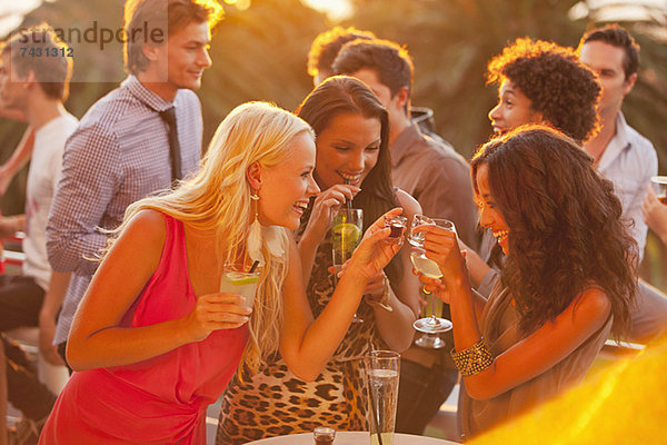 Lächelnde Frauen trinken Cocktails auf dem sonnigen Balkon