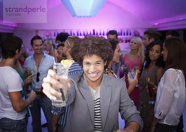 Porträt eines lächelnden Mannes mit Cocktail an der Bar im Nachtclub