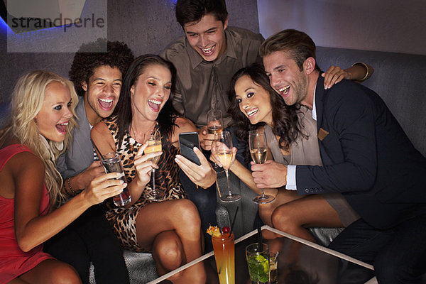 Lächelnde Freunde trinken Cocktails und schauen auf das Handy im Nachtclub.