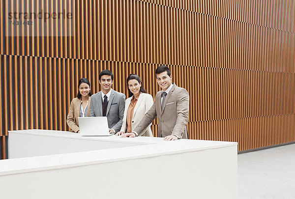 Portrait von selbstbewussten Geschäftsleuten mit Laptop an der Kante im Büro