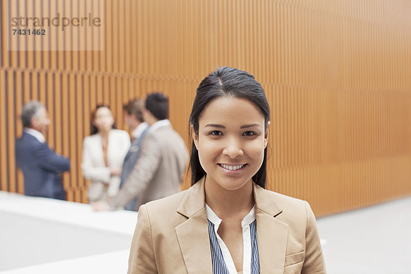 Porträt einer lächelnden Geschäftsfrau mit Mitarbeitern im Hintergrund