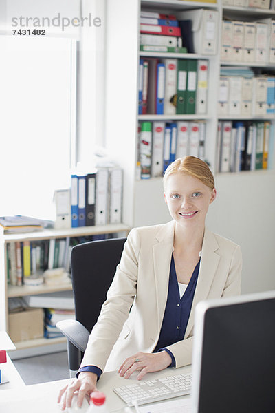 Porträt einer lächelnden Geschäftsfrau am Schreibtisch im Büro