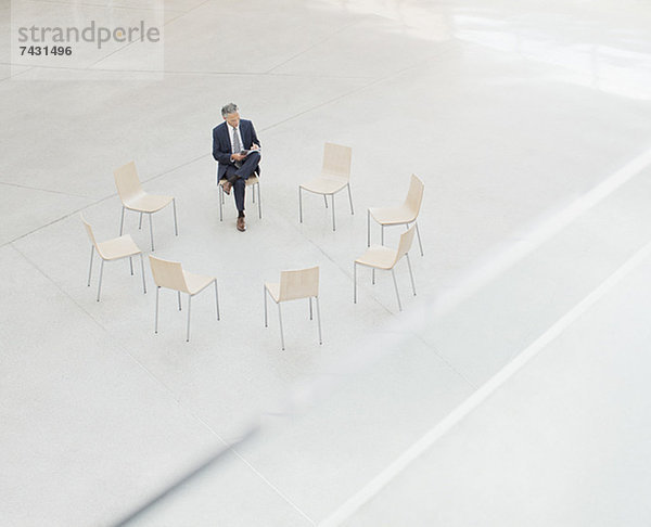 Geschäftsmann  der den Papierkram im Kreis der Stühle in der Lobby überprüft.