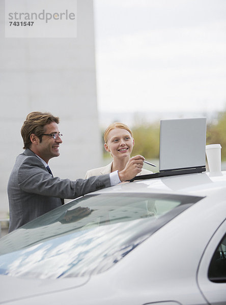 Lächelnder Geschäftsmann und Geschäftsfrau mit Laptop auf dem Auto