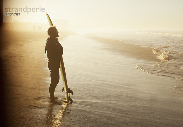 Surfer stehend mit Brett am Strand